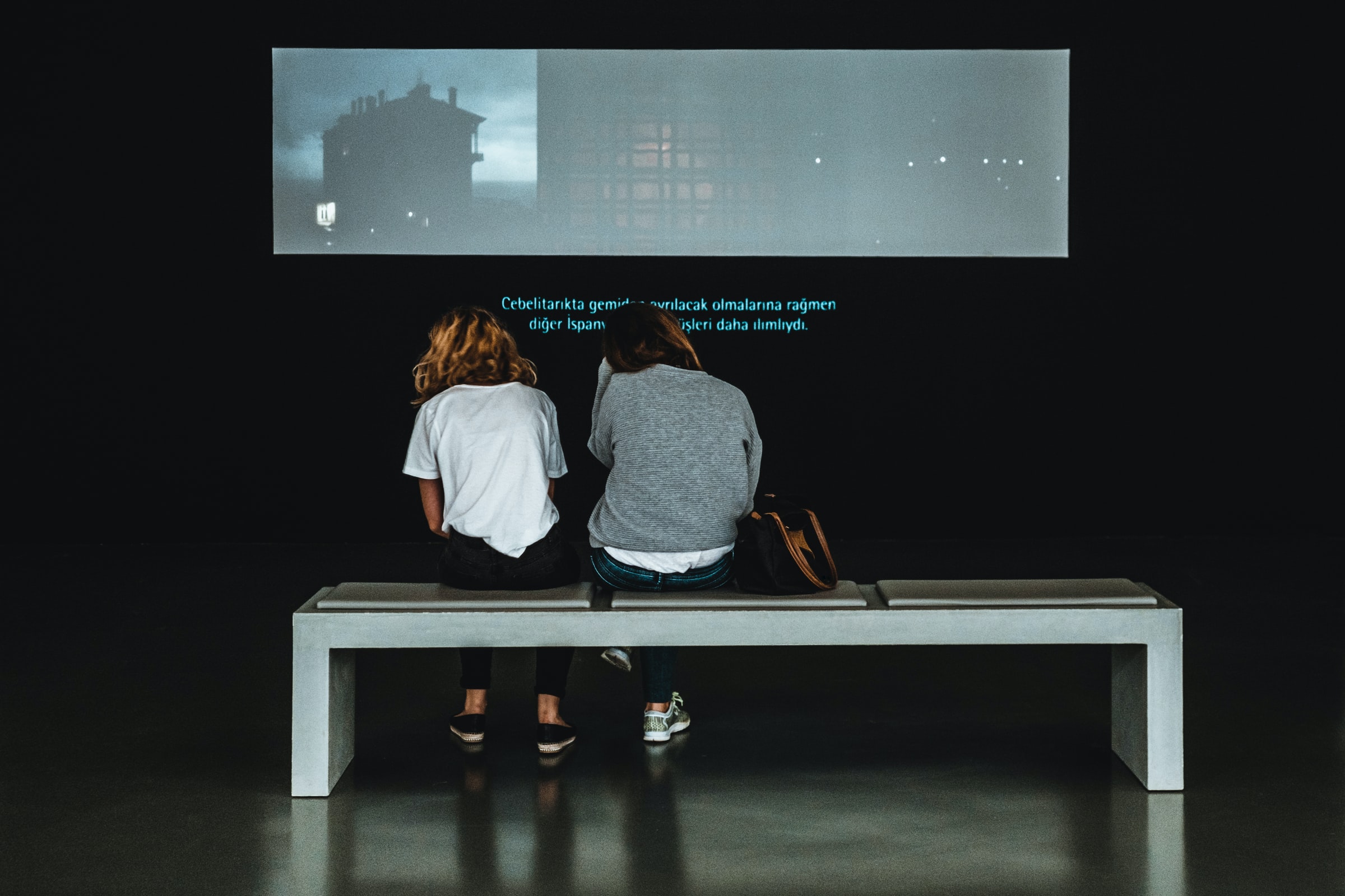 two women sitting in front of a screen with subtitles displayed